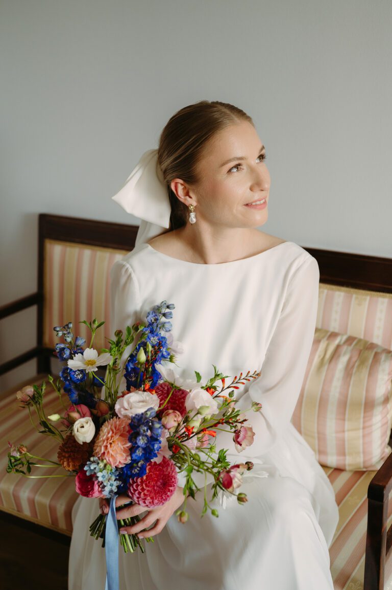Portret uśmiechającej się panny młodej, siedzącej i trzymający bukiet ślubny z pracowni Wykwitnie.