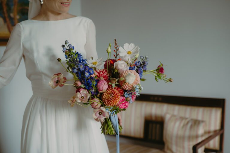 Bukiet ślubny z pracowni florystycznej Wykwitnie. Panna młoda trzyma go w ręce i delikatnie się uśmiecha.