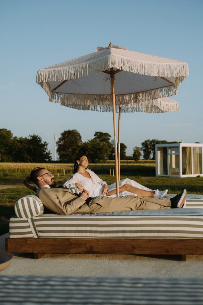 Sesja zdjęciowa w dniu ślubu w Rusiborek Slow. Para młoda leży na leżakach, pod parasolami. Zdjęcia jak poczt&oacute;wka z włoskiego wybrzeża.