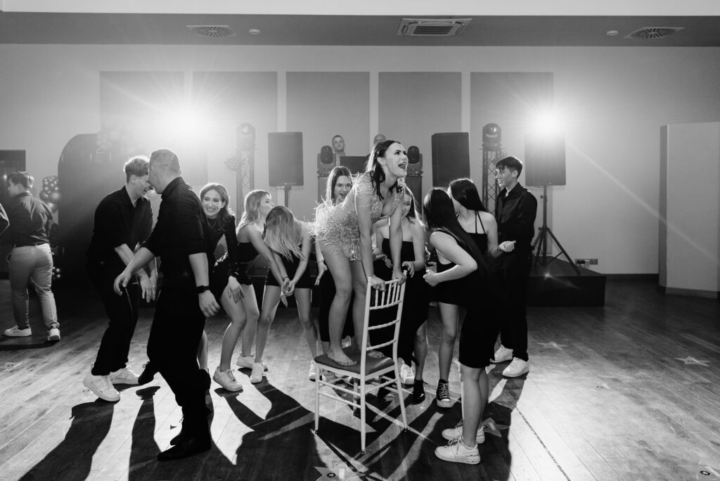 Dziewczyna tańczy na krześle otoczona przyjaci&oacute;łmi podczas swoich 18 urodzin.