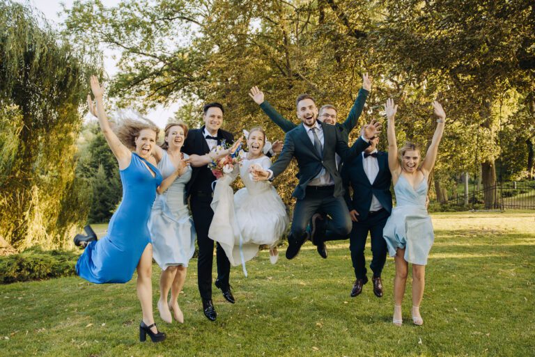 Radosne zdjęcie pary młodej z gośćmi. Wszyscy radośnie wyskakują w g&oacute;rę.