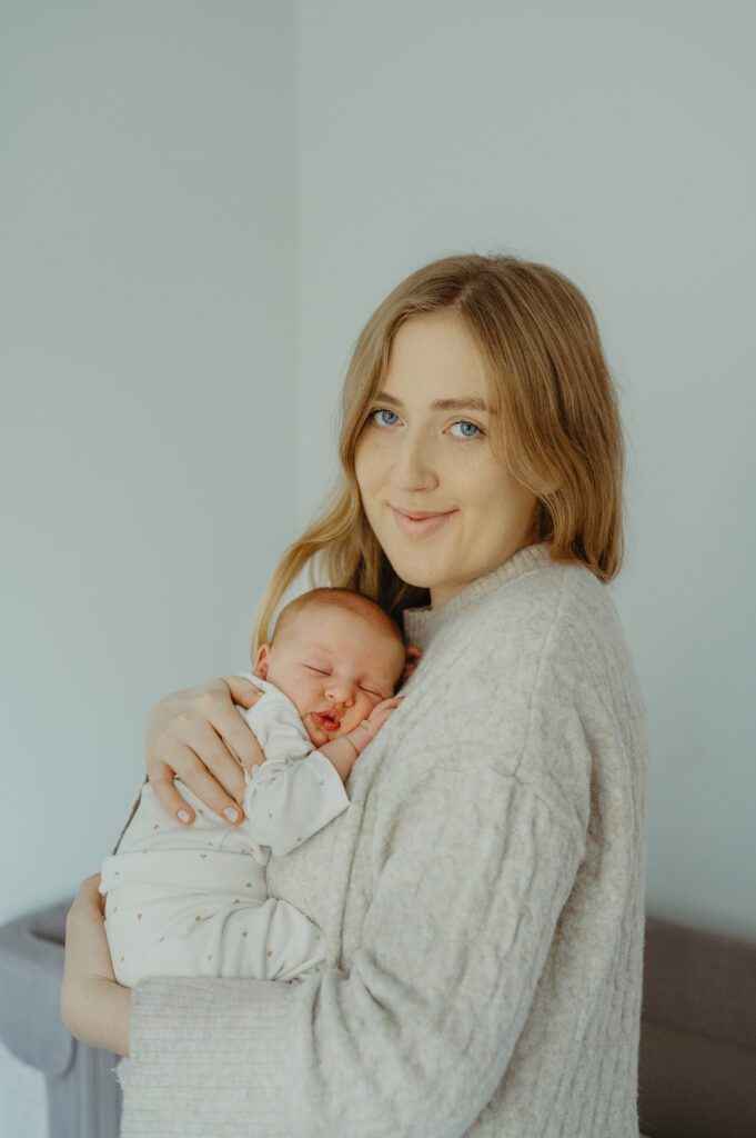 Noworodek w objęciach mamy patrzącej w obiektyw.