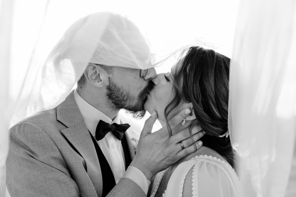 Pocałunek pary młodej pod welonem.