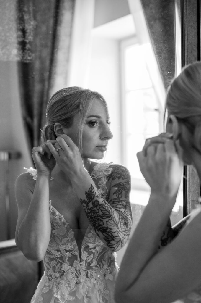 Panna młoda zakłada kolczyki i patrzy w lustro.